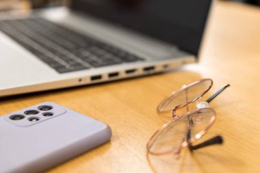 Çalışma alanı ayrıntıları ve nesneler kavramı. Dizüstü bilgisayar gözlükleri ve masada bir kadına ait bir telefon var. Okula ve okul yılına geri dönüyorum.