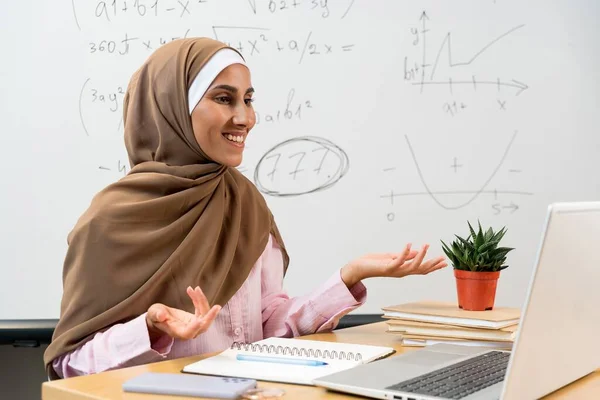 Eラーニングコンセプト ビデオ通話をするヘッドスカーフの女性アラビア語教師の笑顔で 学生に英語の文法規則を説明します 若いイスラム教徒の女性がパソコンの画面を見て机に座っている — ストック写真