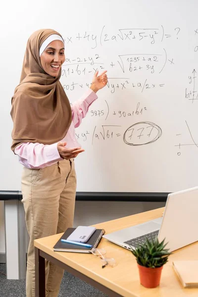 블랙보드 근처에 서있는 무슬림 선생님의 사진은 노트북에 온라인 수업을 학생들에게 로열티 프리 스톡 이미지