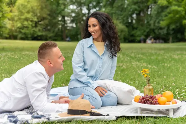 Young man arranged a surprise picnic for his beloved girl in a park in nature. Pleasant conversation in the fresh air, sitting on a blanket. girl of oriental appearance, dressed in jeans and a shirt.