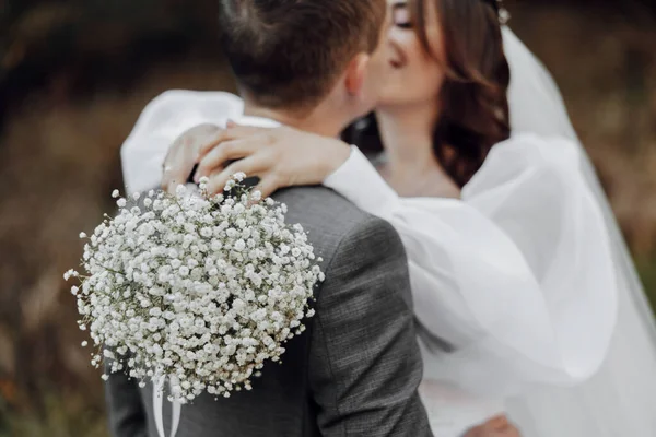 新娘手里拿着一束白色的婚纱 拥抱新郎 温柔地亲吻新娘 — 图库照片