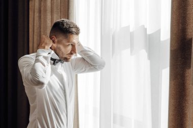 Şık damat elbiselerini giyer, düğün törenine hazırlanır. Büyük bir portre. Sabah ışığında harika bir iç mekan. Damadın sabahı.