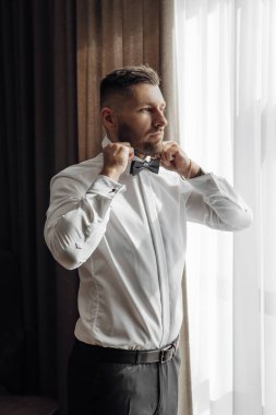 Şık damat elbiselerini giyer, düğün törenine hazırlanır. Büyük bir portre. Sabah ışığında harika bir iç mekan. Damadın sabahı.