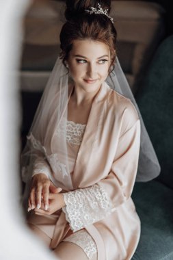 Düğün gününün hassas sabahı. Şık gelinlik içinde siyah saçlı güzel bir gelinin moda fotoğrafı ve düğün sabahı odada poz veren Diadem.