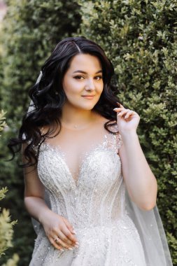 Beyaz elbiseli, uzun kıvırcık saçlı, mutlu bir genç kadın. Parktaki güzel kız kameraya yakından bakıyor.