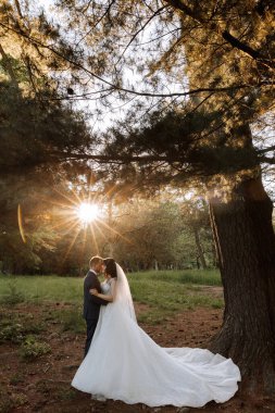 Mutlu genç bir çift, uzun kıvırcık saçlı, beyaz elbiseli, uzun trenli, kalenin yanında güzel çiçekli bir gelin. Parktaki güzel kız. Güzel güneş ışığı. Düğün fotoğrafı çekimi.