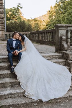 Mutlu genç bir çift, uzun kıvırcık saçlı, beyaz elbiseli, uzun trenli, kalenin yanında güzel çiçekli bir gelin. Parktaki güzel kız. Güzel güneş ışığı. Düğün fotoğrafı çekimi.