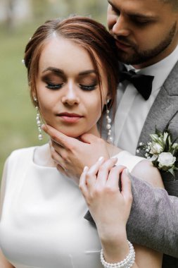 Gelin beyaz bir gece elbisesi içinde damat ile güzel bir saç stili ile poz verir, damat gelini nazikçe sarar ve saç stiline yaslanır.