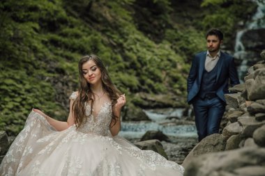 Dağ nehrinin yakınında bir düğün çifti. Ön planda odaklanmış durumda. Damat ve gelin. Doğada düğün fotoğrafı çekimi. Gelin ve damadın ormanında fotoğraf çekimi..