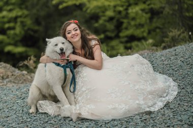 Dağlardaki mutlu evlilik çifti. Uzun saçlı gelin, köpekle samimi bir şekilde gülümsüyor. Doğada düğün fotoğrafı çekimi. Gelin ve damadın ormanında fotoğraf çekimi..