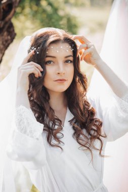 Uzun kıvırcık saçlı güzel bir gelin ve elinde tuttuğu narin bir taç. Objektife bakan bir kızın portresi. Doğal makyaj.