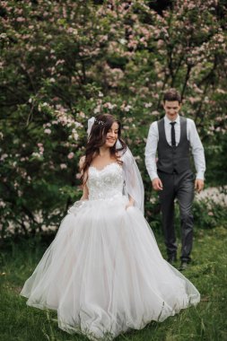 Geline doğru yürürken mutlu şık damat. Gelin ön planda duruyor. Yelek giymiş damat. Damadın portresi. Bahar düğünü