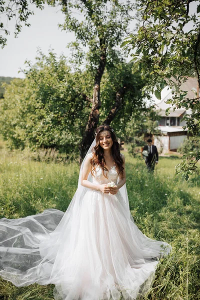 The first wedding meetings in the garden. A meeting of newlyweds on a green field in the open air, a surprise in nature. Front view of smiling bride waiting for groom. Wedding ceremony in the forest.