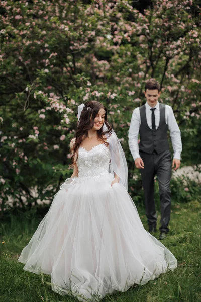 幸せなスタイリッシュな新郎新婦に歩いてください 花嫁は前景にいます ベストを着た新郎 新郎の肖像画 春結婚式 — ストック写真