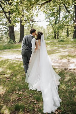 Tarz sahibi genç gelinler, mutlu günlerinde, birbirlerinin keyfini çıkarırlar. Onlar bahar parkında yürüyorlar. Arkadan bir fotoğraf. Bahar düğünü. Doğal makyaj.