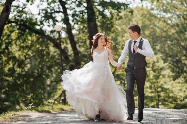 Damat ve gelin bahçede. Parkta bahar düğünü. Parkta koşan mutlu evlilik çifti. Şık ve güzel. Prenses elbisesi.
