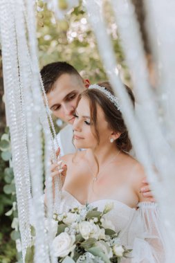 Düğün günü damat ve gelin, dışarıda yürüyüş. Damat geline omuzlarından sarılıyor. İnsanlar mutlu ve gülümsüyor. Birbirini seven mutlu çift birbirine bakıyor.