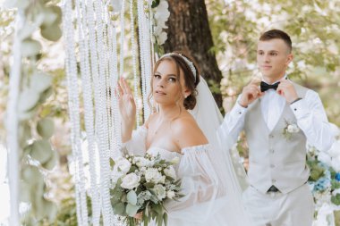 Düğün günü damat ve gelin, dışarıda yürüyüş. Gelin ön planda duruyor. İnsanlar mutlu ve gülümsüyor. Birbirini seven mutlu çift birbirine bakıyor.