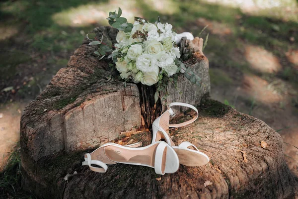 结婚花束在树上 婚礼的细节在公园里的木制树桩上 一束美丽的白花 新娘的鞋子 — 图库照片