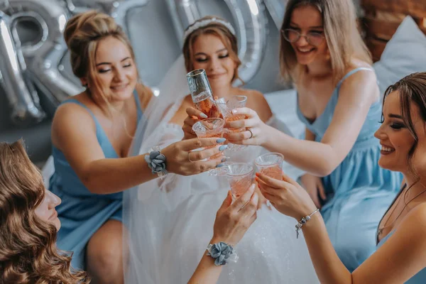 stock image Young bridesmaids in blue silk dresses drink champagne in the bride's room. Beautiful women celebrating bachelorette party sitting on bed and with champagne.