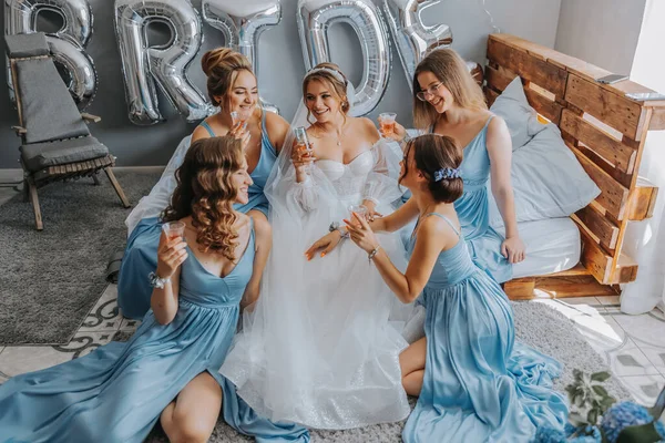 穿着蓝色丝绸衣服的年轻伴娘们在新娘的房间里喝香槟 漂亮的女人坐在床上 喝着香槟 庆祝单身派对 — 图库照片