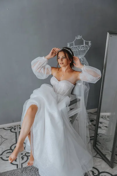白いドレスの美しい巻き毛の花嫁は 袖の美しいドレスのベールの下に立って 写真家のためにポーズをとります 結婚式の写真 クローズアップ肖像画 シックな髪型 — ストック写真
