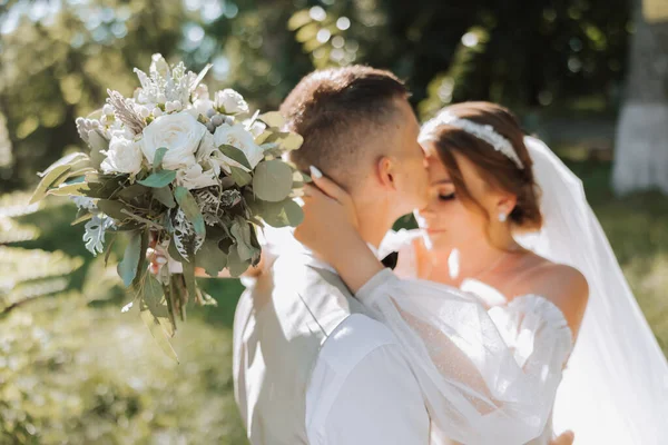 在你的婚礼上 一对美丽的情侣坠入爱河的画像 在公园的阳光和绿叶中散步 新娘和新郎带着一束鲜花的迷人的亲吻和拥抱 — 图库照片