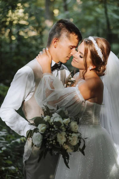 在你的婚礼上 一对美丽的情侣坠入爱河的画像 在公园阳光下散步 新娘和新郎带着一束鲜花的迷人的亲吻和拥抱 — 图库照片