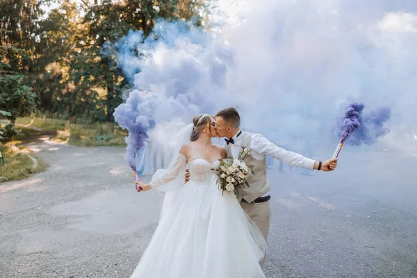 新婚夫妇手里拿着蓝色的多色烟雾弹 新郎和新娘亲吻 结婚快乐 — 图库照片