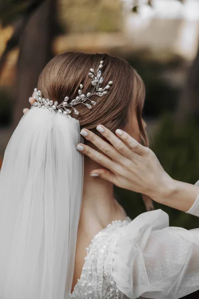 Hairstyle with an elegant wedding hair accessory. Photo from the back. Gently touches the veil. Beautiful and light dress