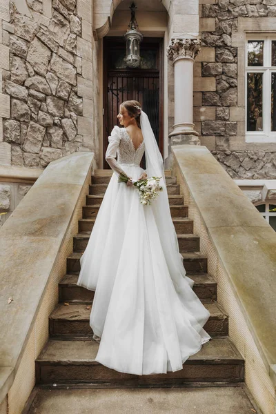 A bride in a dress climbs the stairs. Beautiful lady in a luxurious dress. Graceful bride. The bride climbs the stairs, a dress with a long train