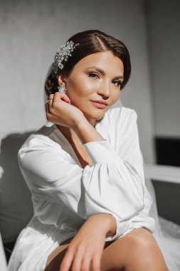 Şık bir düğün aksesuarlı saç stili. Gelin nazikçe dokunur ve küpeleri gösterir. Nazik ve şık bir makyaj.