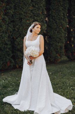 Gelinin elinde bir buket güzel beyaz düğün çiçeği. Parktaki açık hava fotoğrafı. Şık bir gelin. Hassas makyaj.