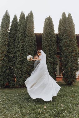 Güzel bir gelini bahar parkında kollarında taşıyan yakışıklı damat. Damat, gelinin kollarında daireler çiziyor.