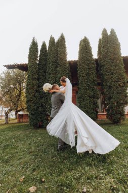 Güzel bir gelini bahar parkında kollarında taşıyan yakışıklı damat. Damat, gelinin kollarında daireler çiziyor.