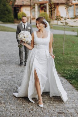 Tarz sahibi genç gelinler, mutlu günlerinde, birbirlerinin keyfini çıkarırlar. Onlar bahar parkında yürüyorlar. Damat gelinin arkasında. Bahar düğünü. Doğal makyaj.