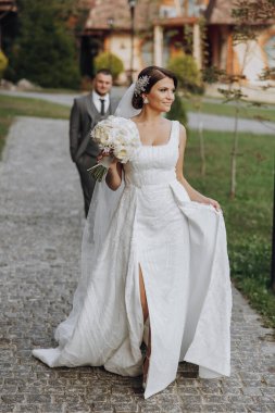 Tarz sahibi genç gelinler, mutlu günlerinde, birbirlerinin keyfini çıkarırlar. Onlar bahar parkında yürüyorlar. Damat gelinin arkasında. Bahar düğünü. Doğal makyaj.