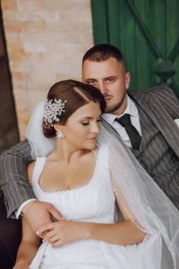 Gelin ve damat yeşil pencerelerin arkasında bir kanepede oturuyorlar. Şık gelin ve damat. Düğün fotoğrafı. kolay atmosfer