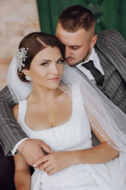 Gelin ve damat yeşil pencerelerin arkasında bir kanepede oturuyorlar. Şık gelin ve damat. Düğün fotoğrafı. kolay atmosfer