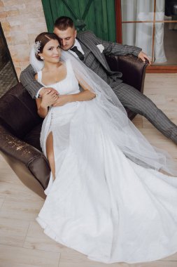 Gelin ve damat yeşil pencerelerin arkasında bir kanepede oturuyorlar. Şık gelin ve damat. Düğün fotoğrafı. kolay atmosfer