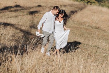 Yazın dağlarda şık bir çift. Beyaz ipek elbiseli genç bir oğlan ve bir kız ormanın arka planında yamaçta yürüyorlar. Kurumuş altın rengi çimenler..