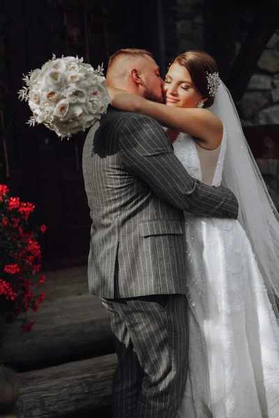 Romantická Nevěsta Bílých Šatech Kyticí Objímá Ženicha Dřevěné Brány Vchodu — Stock fotografie