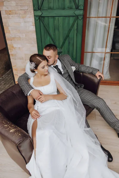 新郎新婦は緑の窓を背景にソファに座っています スタイリッシュな花嫁と新郎 結婚式の写真 気楽な雰囲気 — ストック写真