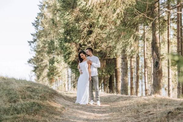 在森林里 穿着白色衣服的时尚模特情侣在日落时接吻 一个女孩拥抱着她的丈夫 头发在风中飘扬 广角照片 — 图库照片