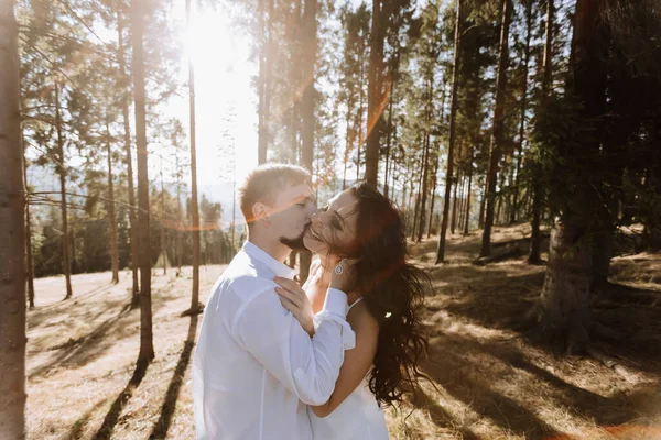 在森林里 穿着白色衣服的时尚模特情侣在日落时接吻 一个女孩拥抱着她的丈夫 头发在风中飘扬 广角照片 — 图库照片