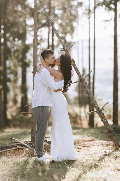 穿着白衬衫的时髦新郎和穿着白衣的可爱的黑发新娘在靠近婚木拱门的森林里 新婚夫妇的婚纱照 — 图库照片