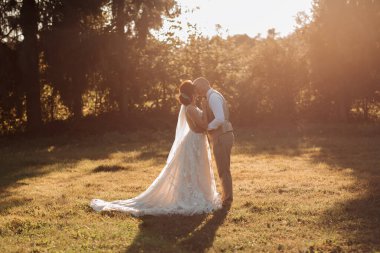 Düğün fotoğrafı. Gelin ve damat güzel bir ormanda, güzel bir ışıkta, sarılıp öpüşüyorlar. Birbirine aşık bir çift. Şık damat