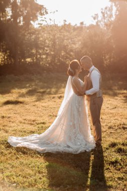 Düğün fotoğrafı. Gelin ve damat güzel bir ormanda ve güzel bir ışıkta duruyorlar, birbirlerine sarılıyorlar ve burunlarını birbirlerine yaslıyorlar. Birbirine aşık bir çift. Şık damat