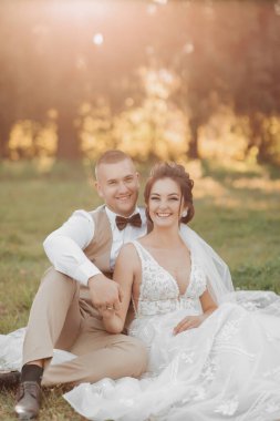 Gelin ve damadın düğün portresi. Mutlu yeni evliler yeşil çimlerin üzerinde el ele tutuşup poz veriyorlar. Şık damat. Güzel genç gelin