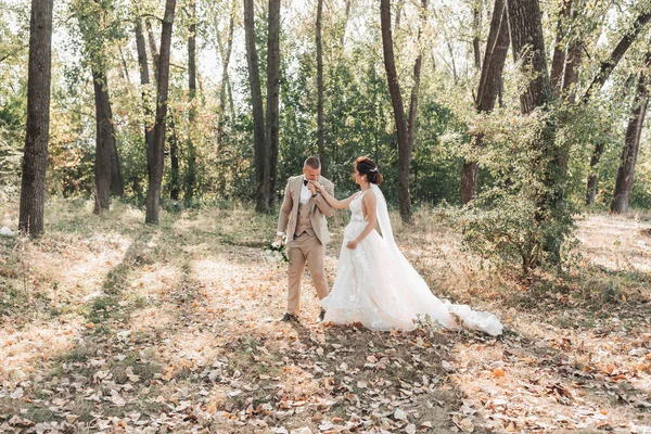 婚纱照新娘和新郎在森林里散步 新郎捧着一束花 吻着他心爱的人的手 长婚纱恋爱中的情侣夏光 — 图库照片